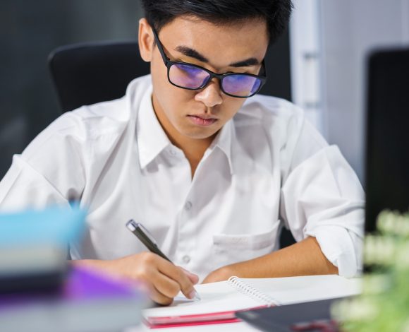 Asian male with glasses writing at computer | Physics