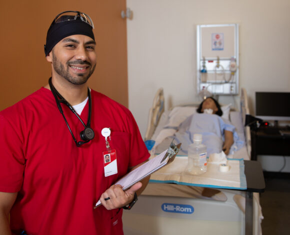 TSTC Nursing student poses wearing red scrubs and a stethoscope while holding a clipboard.
